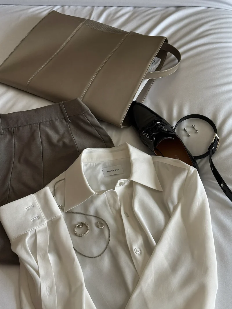 Komplet outfit med sko, bælte og smykker lagt klar på en redt seng